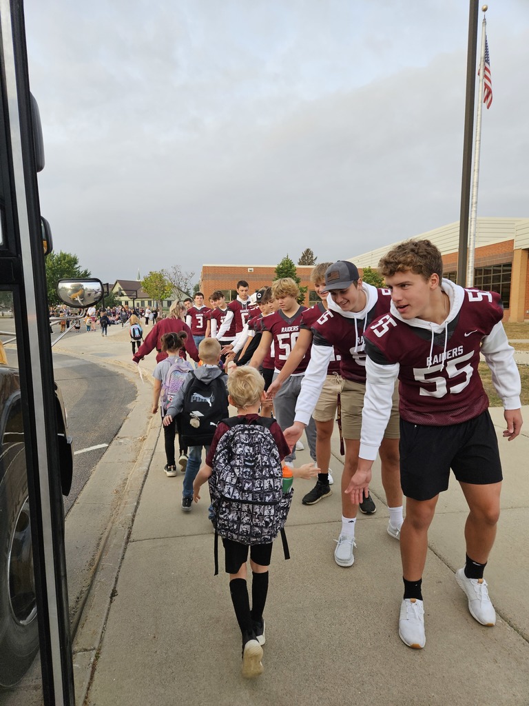 Football players greeting younger students as they get off the bus