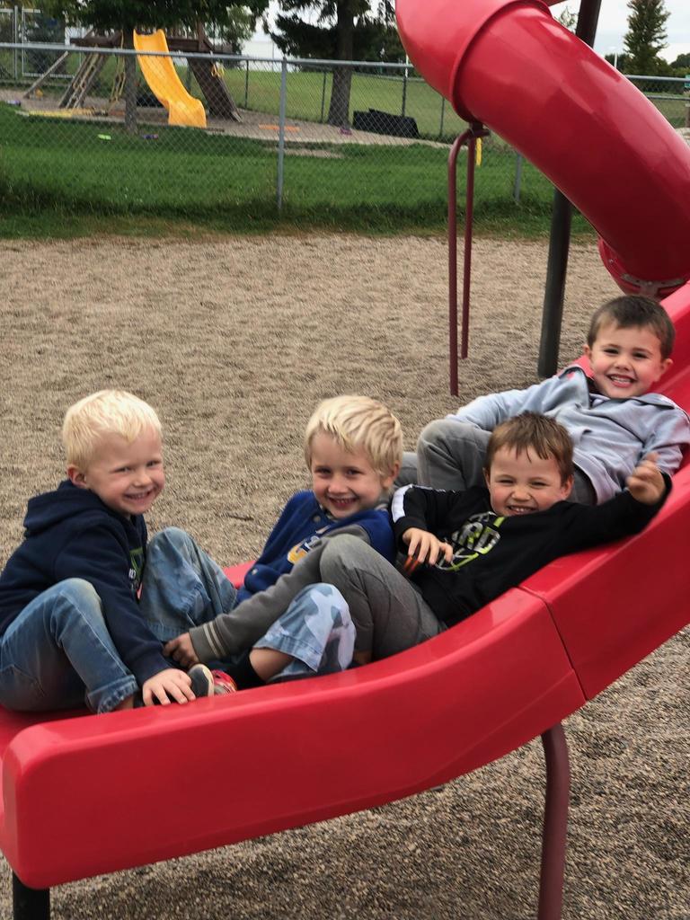 Boys laying on a red slide outside.